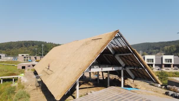 Taket på ett stort hus med torr halm och hö. Arbetstagare som installerar taket. — Stockvideo