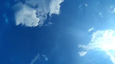 Havuzun dibinden mavi gökyüzü manzarası. Havuzda dalgalar ve kabarcıklar ve sudan geçen güneş ışınları. Arkaplan veya doku