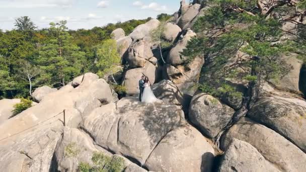 Wedding couple in mountain rock from drone. Aerial view Happy newlyweds in love hugging standing on top of the mountain. — Stock Video