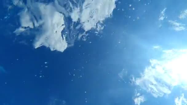 Vy över den blå himlen från botten av poolen. Vågor och bubblor i poolen och solstrålarna passerar genom vattnet. Bakgrund eller struktur — Stockvideo