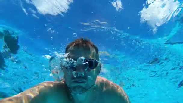 Zamknij twarz człowieka, który pływa pod wodą i zdejmuje twarz. Mężczyzna uwalnia powietrze przez nos pod wodą w basenie.. — Wideo stockowe