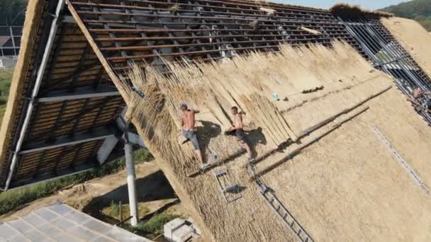 Légi kilátás a tetőn egy nagy ház száraz szalma és széna. A tetőt beszerelő munkavállalók. — Stock videók