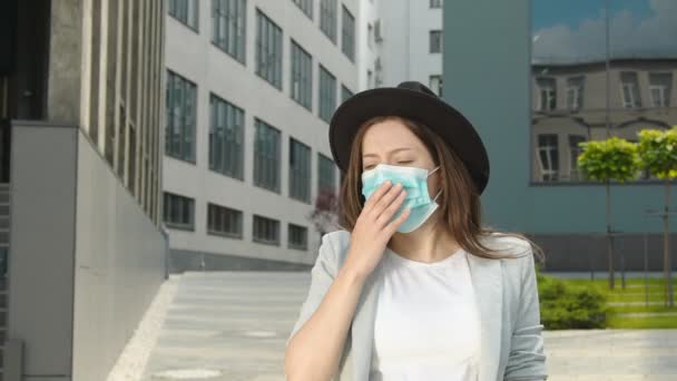 Une femme portant un masque médical marchant dans la rue et toussant. Une femme avec des signes de maladie tousse et se couvre la bouche avec sa main. Toux sèche chez les femmes de la rue. — Video