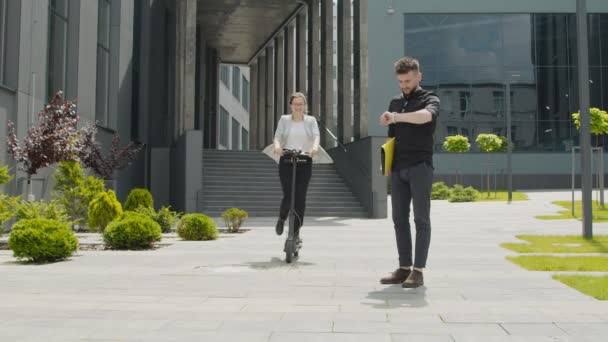 Un homme attend une femme qui arrive sur un scooter électrique. Des hommes et des femmes d'affaires réunis dans la rue. Amis et hommes d'affaires se saluent à la réunion et communiquent joyeusement. — Video