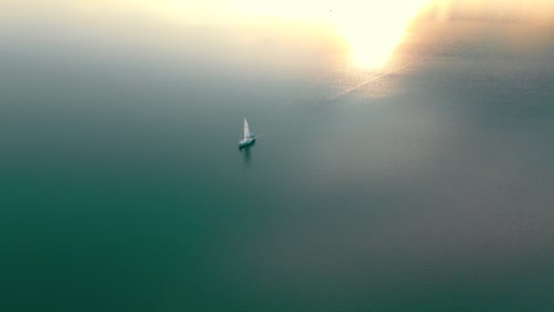 Vista aerea Uno yacht al tramonto in mare aperto. Volo al tramonto vicino allo yacht con vista sulla vela da un'altezza. Il sole si riflette nell'acqua. — Video Stock