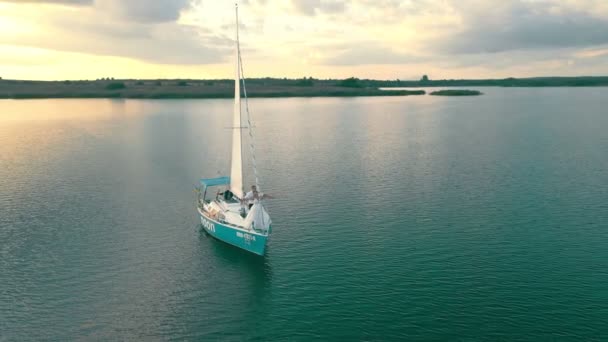 Un yate en el mar desde una vista de pájaro al atardecer. El cielo se refleja en el agua. Vuelo al atardecer cerca del yate con vistas a la vela desde una altura — Vídeo de stock