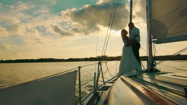 Les jeunes mariés se tiennent sur un arc d'un voilier comme à Titani. Mariés sur un fond de beau coucher de soleil — Video
