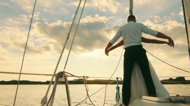 Los recién casados están en una proa de un yate de vela como en Titani. Recién casados sobre un fondo de hermosa puesta de sol — Vídeo de stock