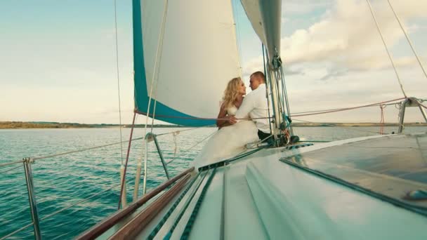 A friss házasok a tavon vitorláznak a jacht fedélzetén. Élvezik egymást, néznek és mosolyognak. — Stock videók