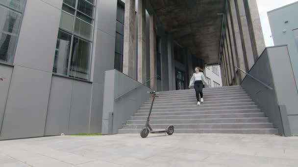 Een jonge vrolijke vrouw benadert een elektrische scooter en huurt hem met een smartphone. Scooter verhuur ontgrendelen met een smartphone. gelukkig vrouw op elektrische scooter — Stockvideo