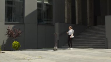 Genç ve mutlu bir kadın elektrikli bir scooter 'a yaklaşır ve onu akıllı bir telefonla kiralar. Scooter kiralama akıllı telefondan açılıyor. Elektrikli scooterlı mutlu kadın