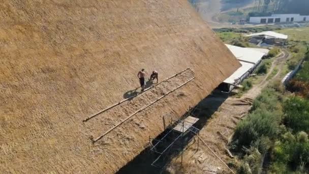 Luftaufnahme vom Dach eines großen Hauses mit trockenem Stroh und Heu. Arbeiter, die das Dach einbauen.
