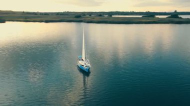 Ukrayna. Lviv. 19.09.2020. Gün batımında kuş bakışı deniz manzaralı bir yat. Gökyüzü suya yansıyor. Gün batımında yelkene tepeden bakan yatın yanında.