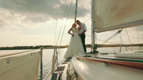 新婚旅行はタイターニのようなセーリングヨットの弓の上に立っています。美しい夕日を背景に新婚旅行 — ストック動画