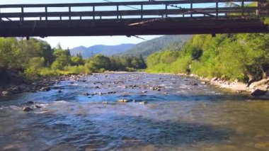 Nehrin üzerinde tahta bir köprünün altından uçmak. İnsansız hava aracı köprünün altından uçuyor ve nehrin ve kayaların üzerinden alçaktan uçuyor..