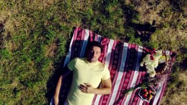 Aerial Top Manzarası. Genç bir çift, yeşil çimlerde uzanan ve öpüşen gençlere aşık. Kız, erkeğin yanına uzanıp ona sarılıyor..