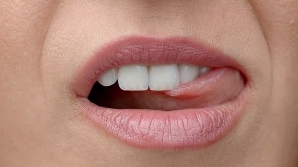 Kvinnan slickar läpparna på nära håll. Skonsam kvinnlig tunga slickar vackra vita tänder. — Stockvideo