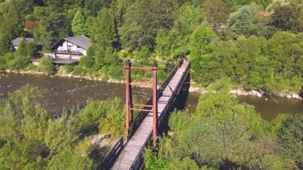 Uitzicht vanuit de lucht vanaf een oude houten hangbrug over een bergrivier. Meisje dat op een houten brug staat en naar de toekomst kijkt. Bestraffende landschap van een berg rivier op een zonnige dag. — Stockvideo