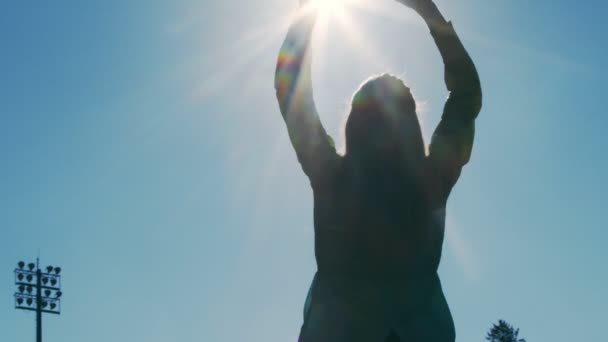 Silhouet van een vrouwelijke atleet in het stadion kneden op een achtergrond van blauwe lucht. Opwarmen in het stadion voor de start van sportwedstrijden. — Stockvideo