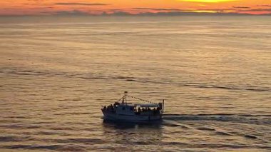 Rovinj Hırvatistan 'da altın gün batımında Adriyatik Denizi' nde yelken açan yolcularla dolu bir tekne, sıcak renklerle dolu ve seyahat atmosferi yaratan dramatik bir ufuk..