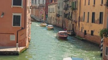 Venedik 'teki dar kanallarda su taksileri geziyor. İtalya 'da güneşli bir günde, renkli tarihi binalarla dolu dar bir Venedik kanalından çok sayıda su taksisi geçiyor.