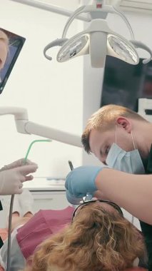 Bir diş hekimi ve koruyucu maskeli asistanı bir diş kliniğinde hastaların dişlerini tedavi eder. Sağlık ve tıp konsepti. Modern diş sağlığı kliniği.