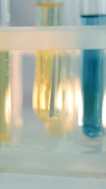 Laboratuvarda mavi ve sarı maddeli test tüpleri var. Laboratuvarda çalış. Bir laboratuvar teknisyeni test tüplerini yakın plan bir tripoda koyar..