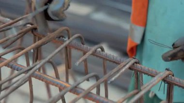 İnşaat işçisi inşaat demirini kablolarla bağlıyor, Eldivenlere Kapanıyor, Beton Vakfı için sağlam bir çerçeve oluşturuyor, İnşaat alanında endüstriyel süreç.