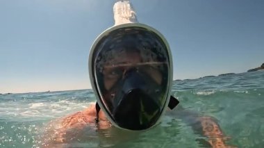 Güneşli yaz gününde açık deniz suyunun yüzeyinde yüzen maskeli adam..