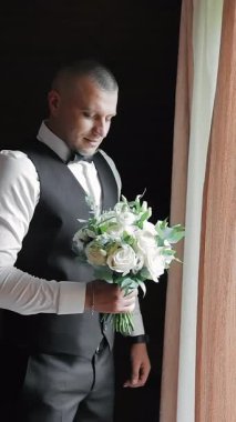 Bir adam kız arkadaşına hediye olarak elinde lüks bir buket çiçek tutar. Damat düğün gününde gelin buketini pencerede tutar..