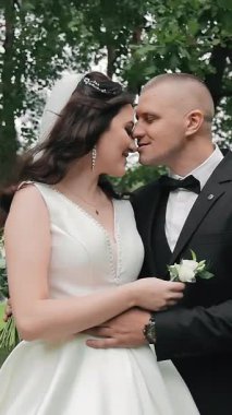 Düğün günlerinde genç bir çift parkta sarılıyorlar. Mutlu yeni evliler birbirlerine şefkat ve dokunmaktan zevk alırlar.