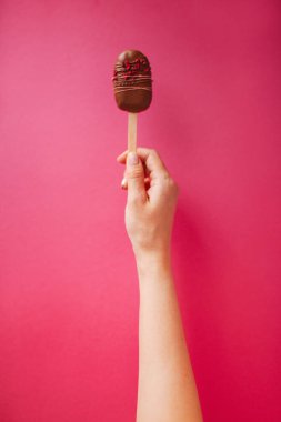 Elinde pembe bir arka plan üzerinde popsicle kek
