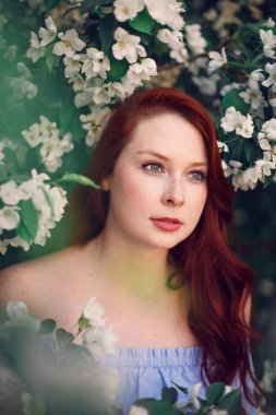 Çiçek açan elma ağacında poz veren kızıl saçlı bir model..