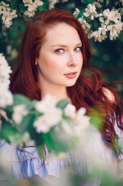 Çiçek açan elma ağacında poz veren kızıl saçlı bir model..