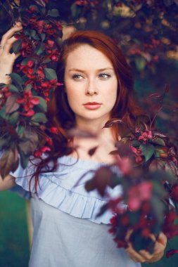Çiçek açan elma ağacında poz veren kızıl saçlı bir model..