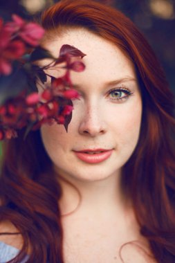 Çiçek açan elma ağacında poz veren kızıl saçlı bir model..