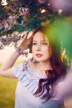 Kızıl saçlı manken yazın çiçek açan leylakların içinde poz veriyor..