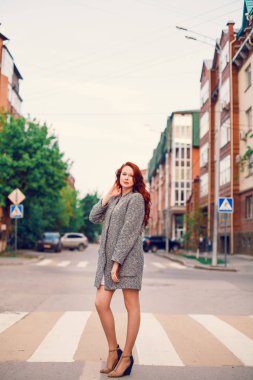 Sokakta gün batımının arka planında poz veren kızıl saçlı bir manken..