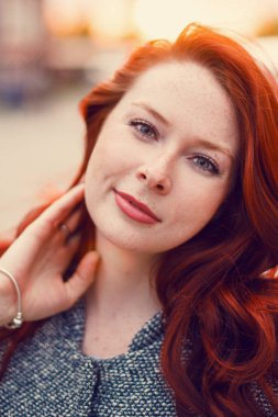 Sokakta gün batımının arka planında poz veren kızıl saçlı bir manken..