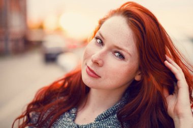 Sokakta gün batımının arka planında poz veren kızıl saçlı bir manken..