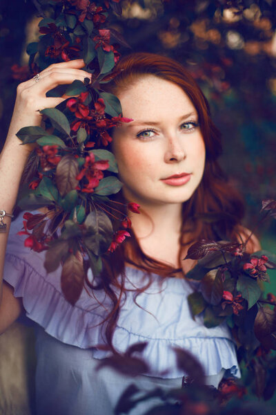 Model with red hair posing in a blooming apple tree.