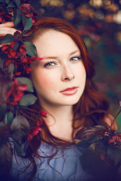 Model with red hair posing in a blooming apple tree.