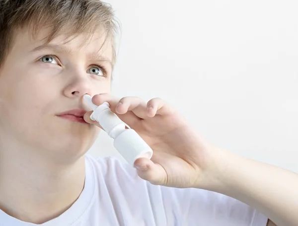 Adolescente freddo utilizzando spray nasale primo piano su uno sfondo bianco — Foto Stock