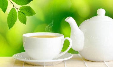 Ahşap masa üzerinde yeşil çay ve beyaz seramik çaydanlık fincan.