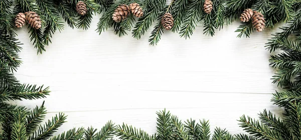 Christmas frame of fir branches and pine cones on white wooden board — Stock Photo, Image