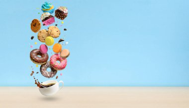 Donuts, cupcakes, cookies, macaroons and coffee cup flying over blue background. . Sweetshop and coffeeshop concept background. Copy space.