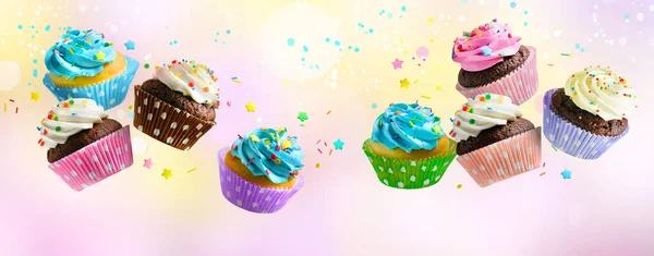 Cupcakes with pink white and blue cream and colorful sprinkles flying over pink abstract background. — Stock Fotó