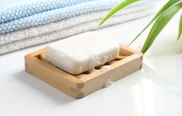 Biały mydło bar z pianką na drewnianej misce mydlanej i bawełniane ręczniki na białym stole. — Zdjęcie stockowe