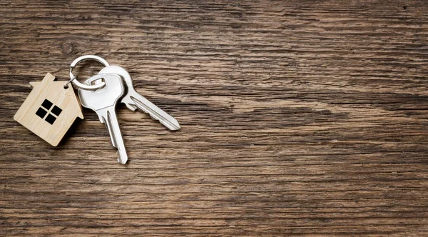 Eski ahşap dokulu arka planda ev şeklindeki anahtarlığı olan ev anahtarı çifti. Üst Manzara. Boşluğu kopyala