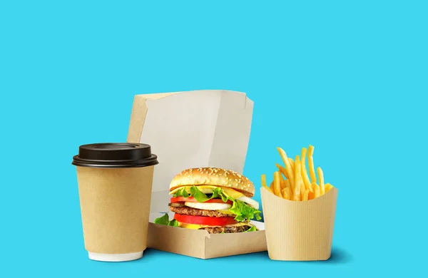 Fast food lunch delivery. Tasty Hamburger, fries and coffee in cardboard package on blue background. — Stock Photo, Image